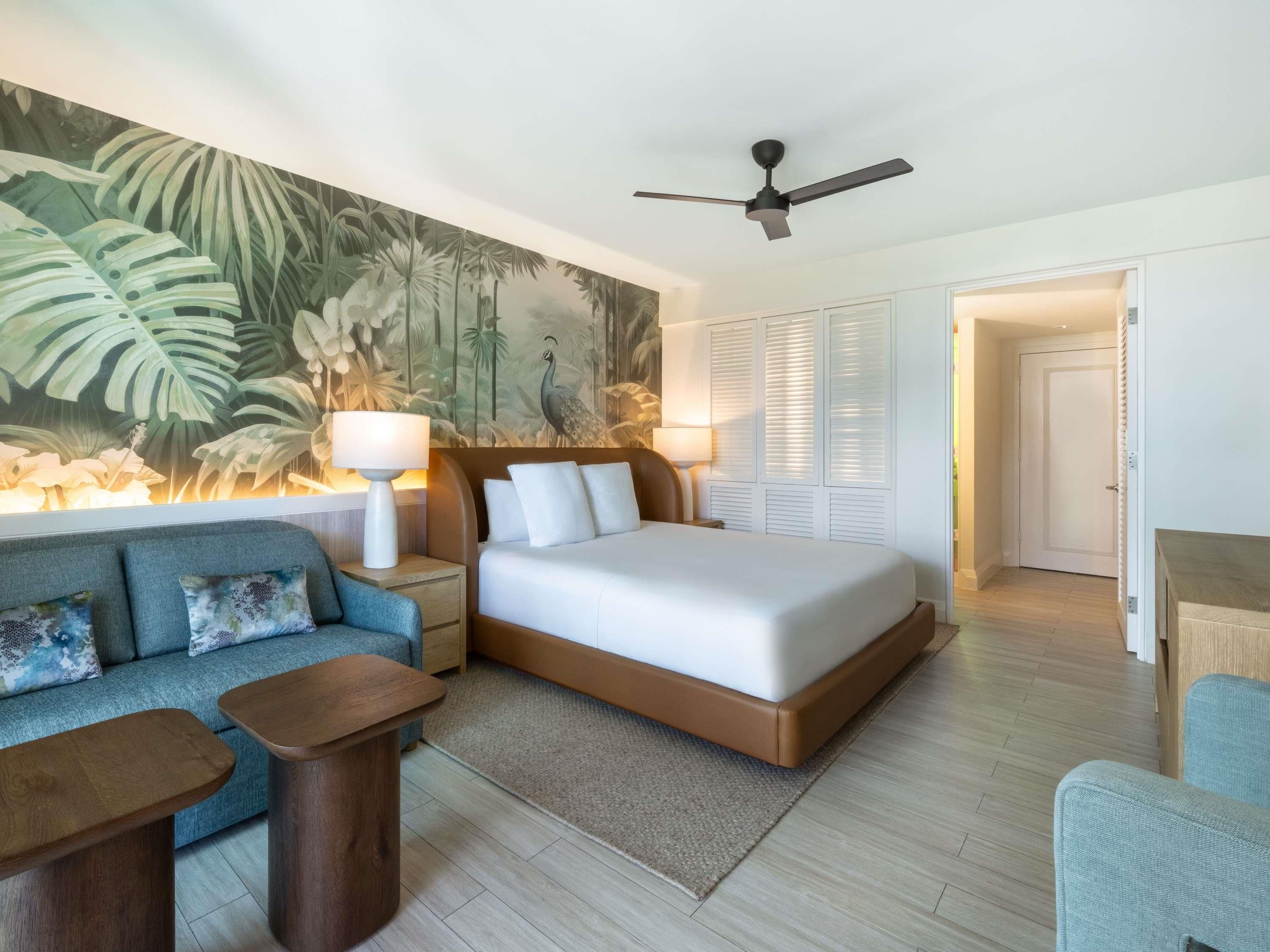 A modern hotel room with a large bed, a sofa, a coffee table, and a ceiling fan.