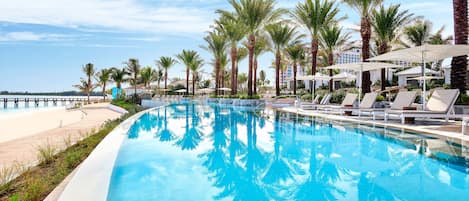 A swimming pool with lounge chairs and palm trees, surrounded by a hotel building.