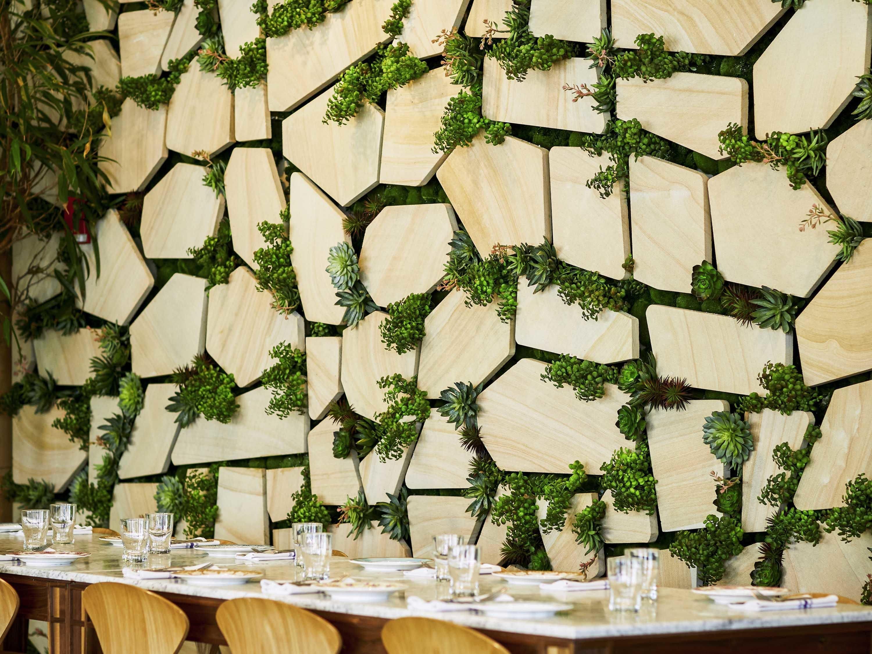 Un comedor con una mesa dispuesta para cuatro personas, rodeado de paneles de madera hexagonales con plantas.