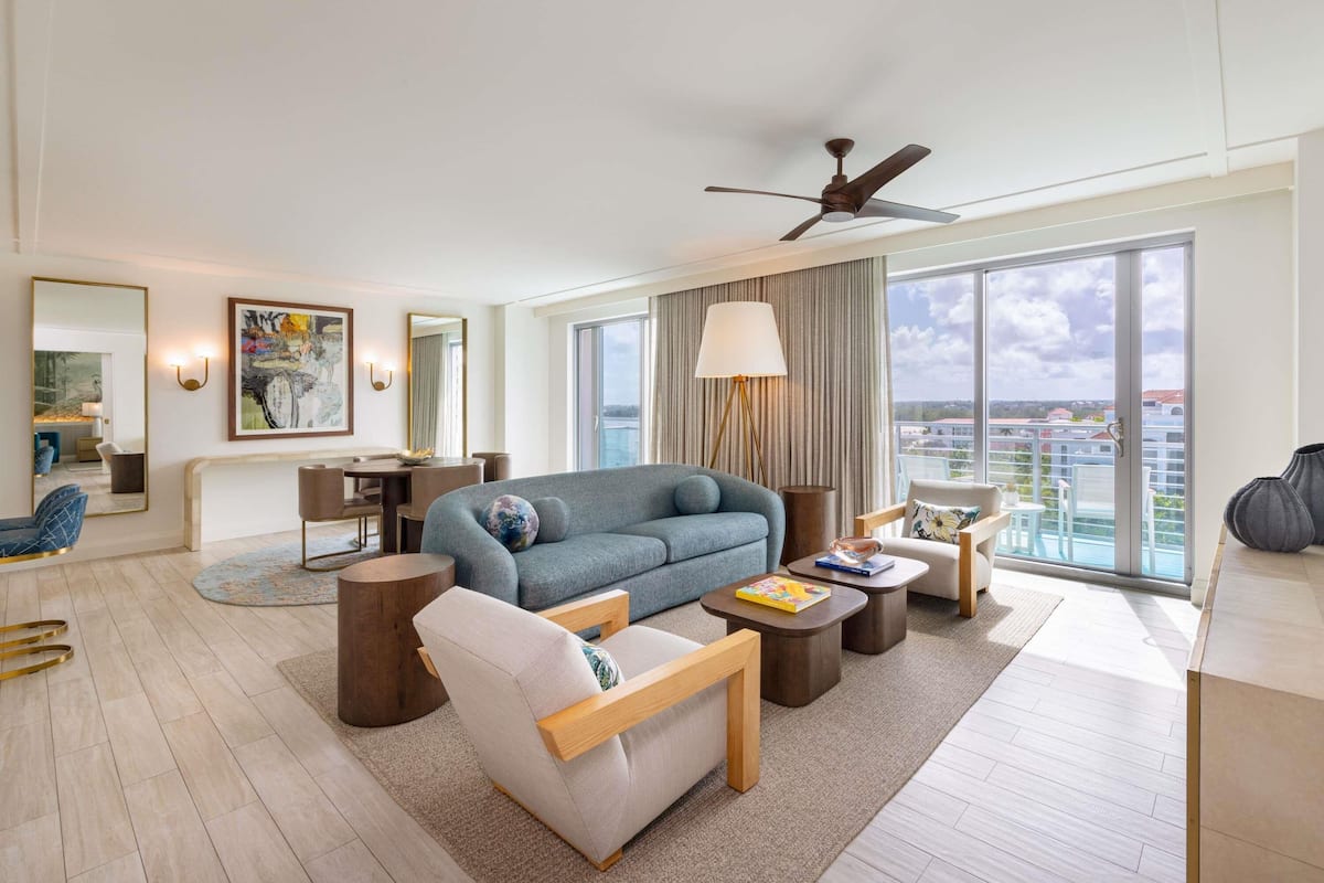 A modern hotel room with a large sofa, a coffee table, a side table, a lamp, and a ceiling fan.