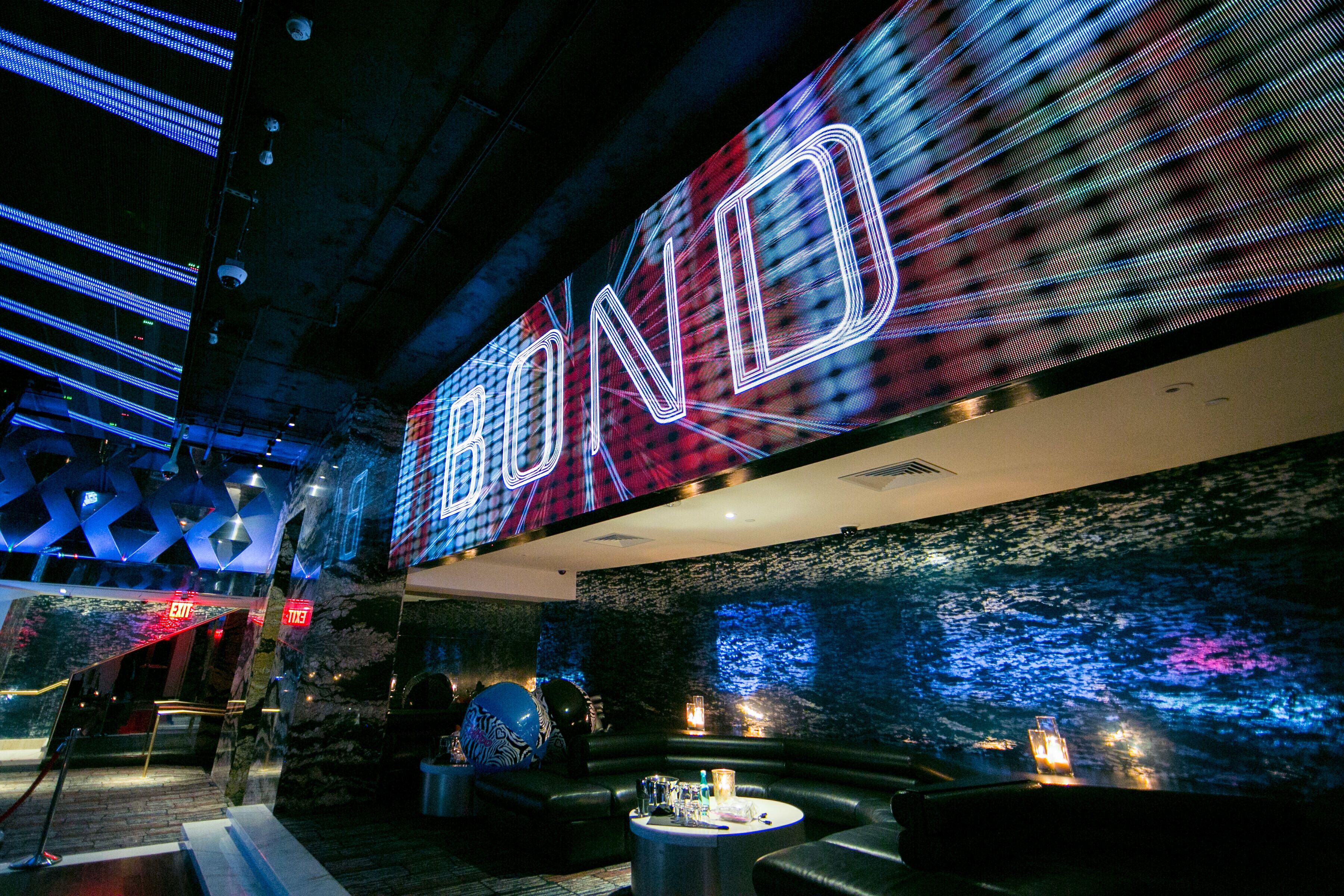 Een moderne lounge met een groot LED-bord, comfortabele zithoek en een decoratieve wand.