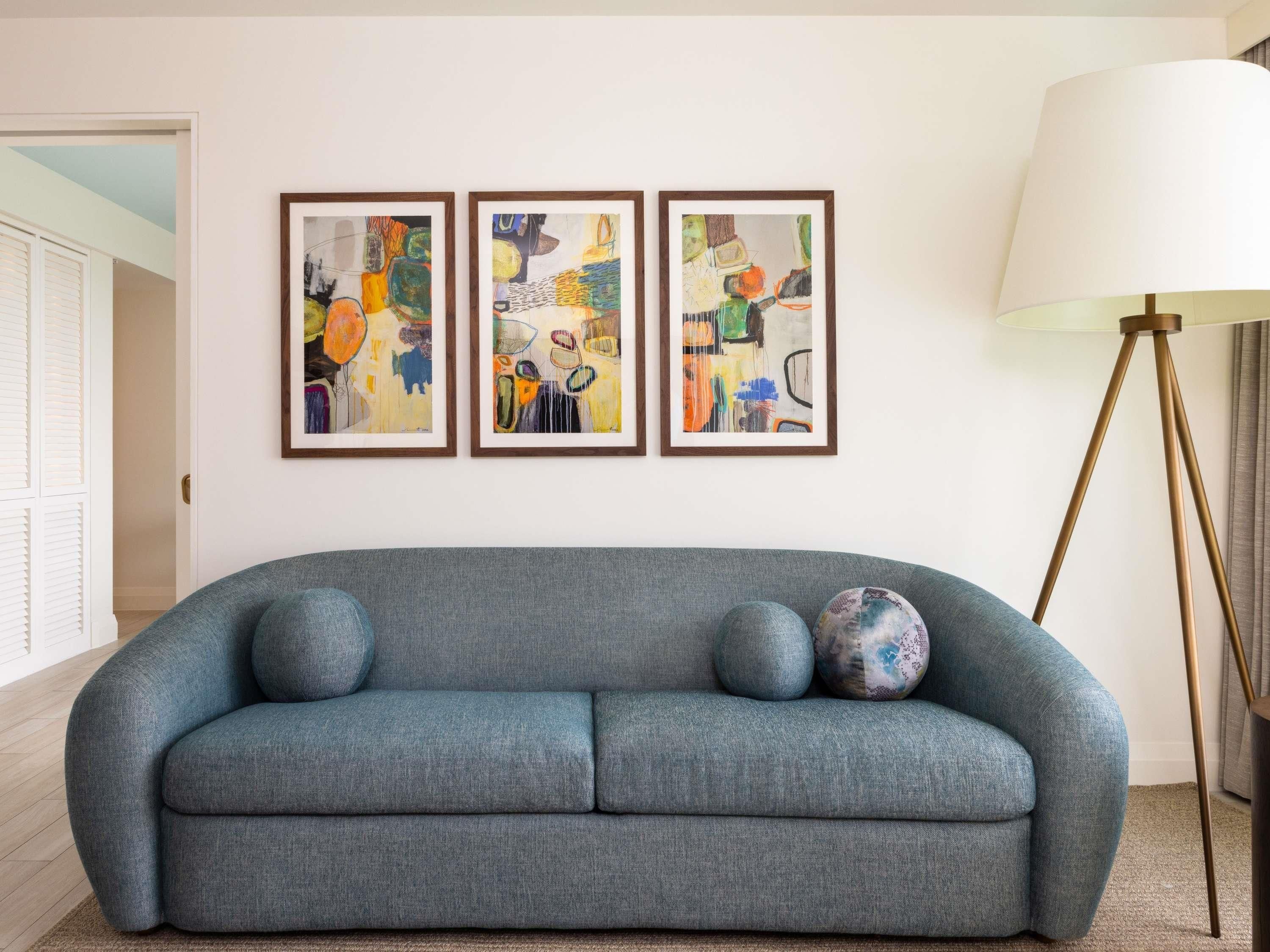 Una sala de estar moderna con un sofá gris, tres cuadros abstractos enmarcados y una lámpara de pie.