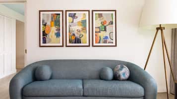Una sala de estar moderna con un sofá gris, tres cuadros abstractos enmarcados y una lámpara de pie.