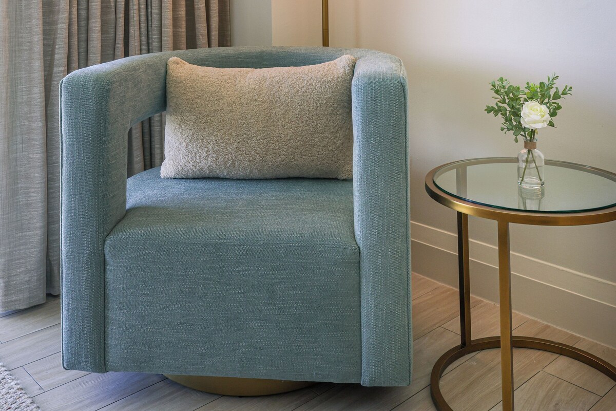 A room with a blue armchair, a round table with a glass top, and a floor lamp.