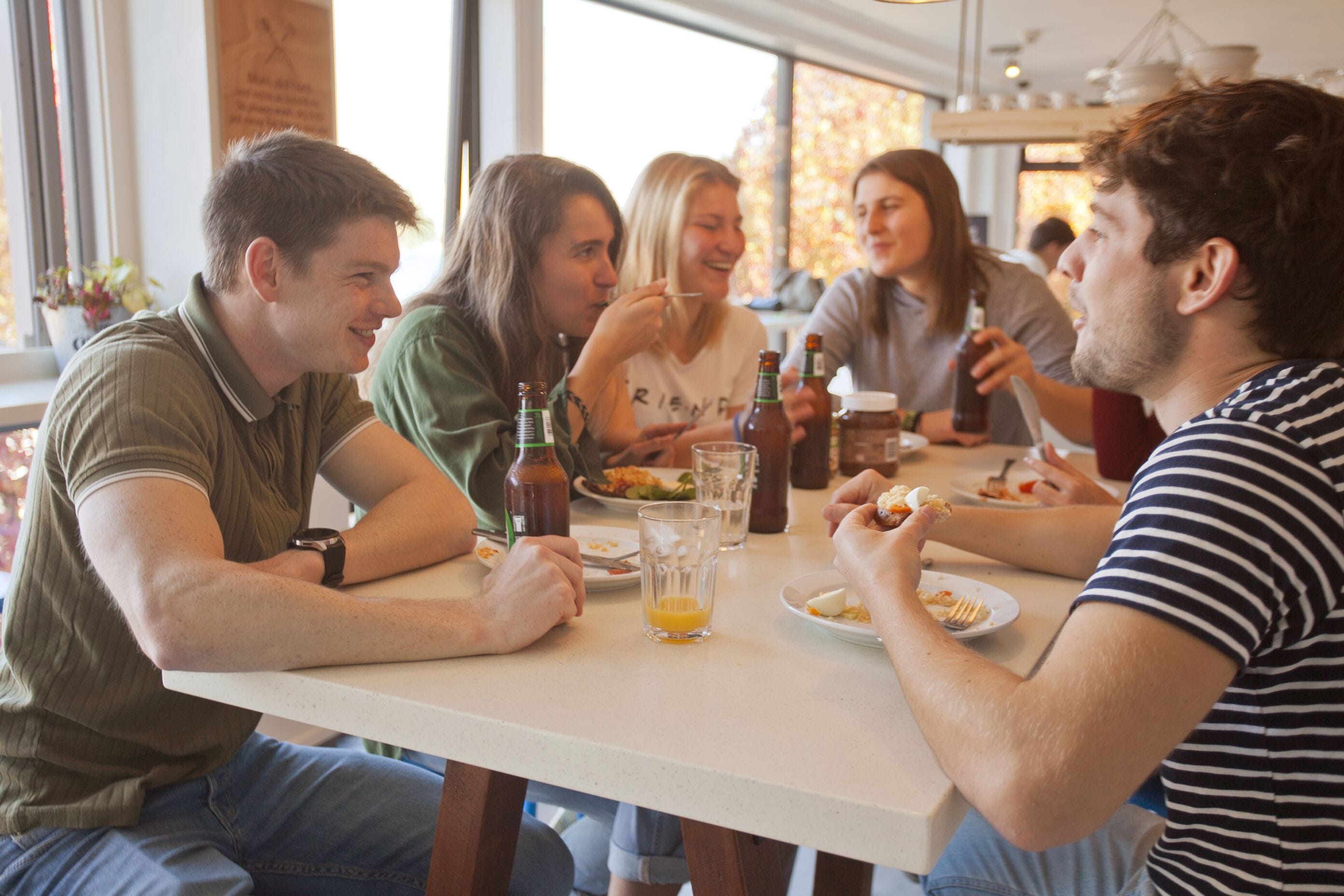 A group of people dining at a table in a well-lit indoor setting with large windows.