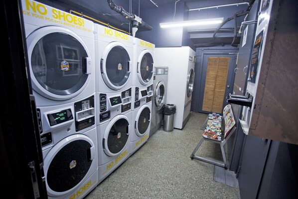 A laundromat with multiple washers and dryers, a trash bin, and a magazine rack. - Absoloot Hostel Queenstown (Queenstown)