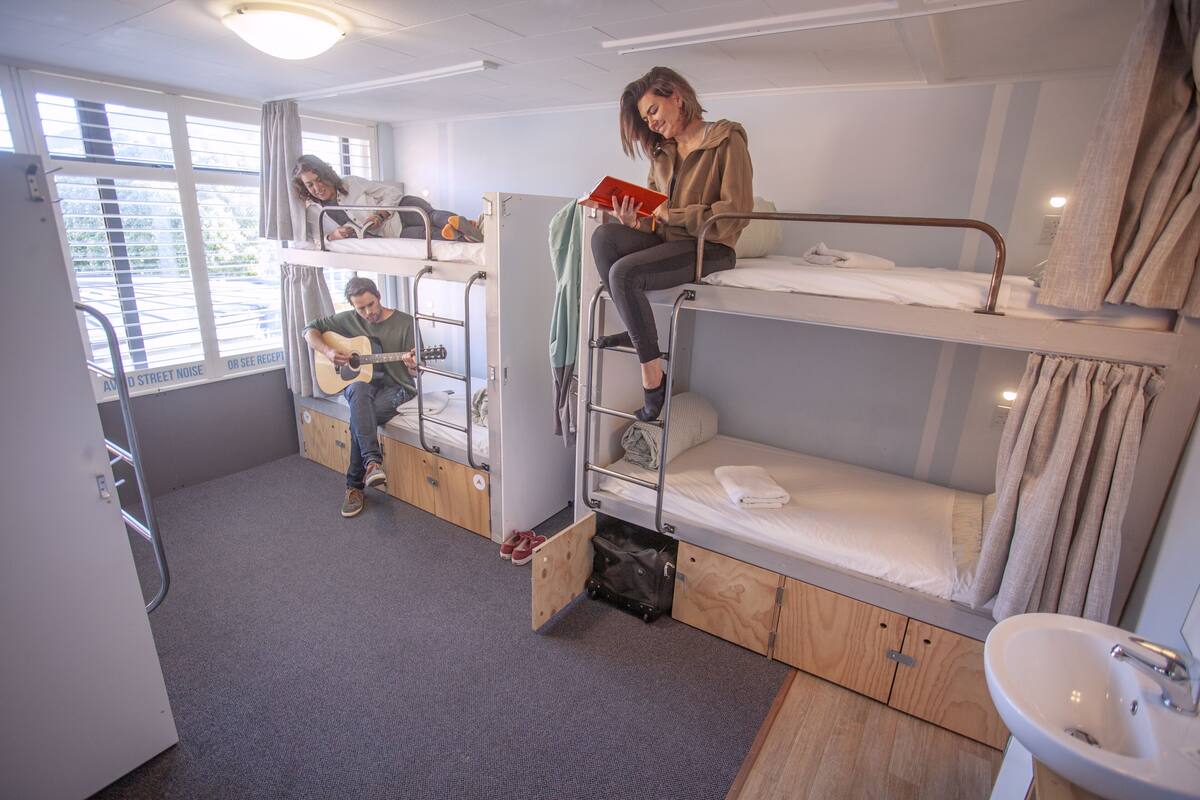 A dormitory room with bunk beds, a sink, and a window with curtains.