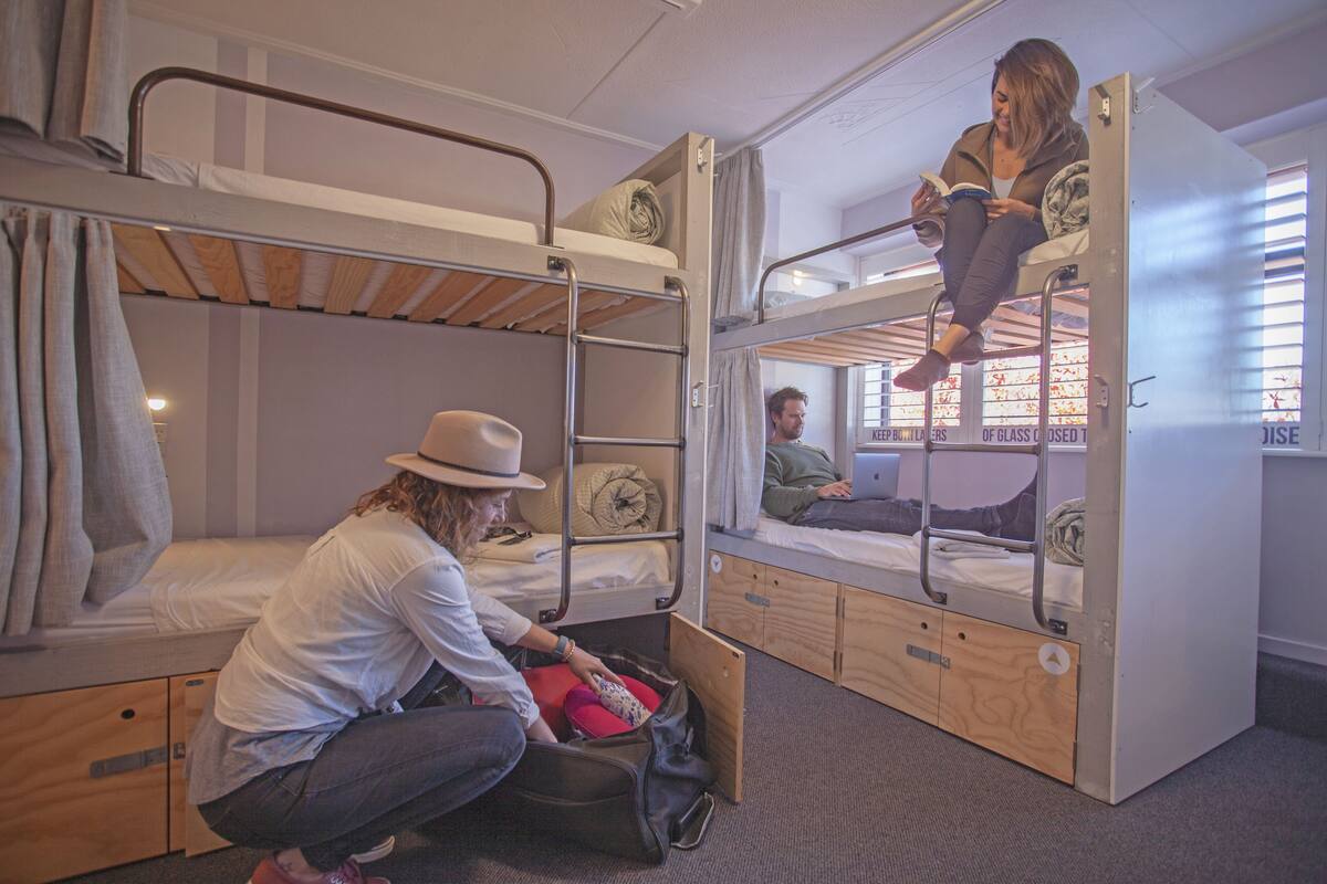 A dormitory room with bunk beds, a suitcase, and a laptop on one of the beds.