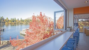 Un intérieur moderne avec une grande fenêtre donnant sur un lac et les couleurs automnales des arbres.