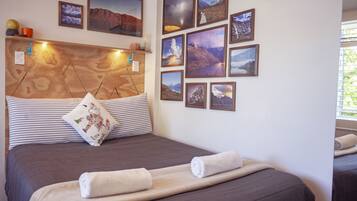 A hotel room with a wooden headboard, multiple framed pictures on the wall, a bed with two pillows, and two rolled towels on the bed.