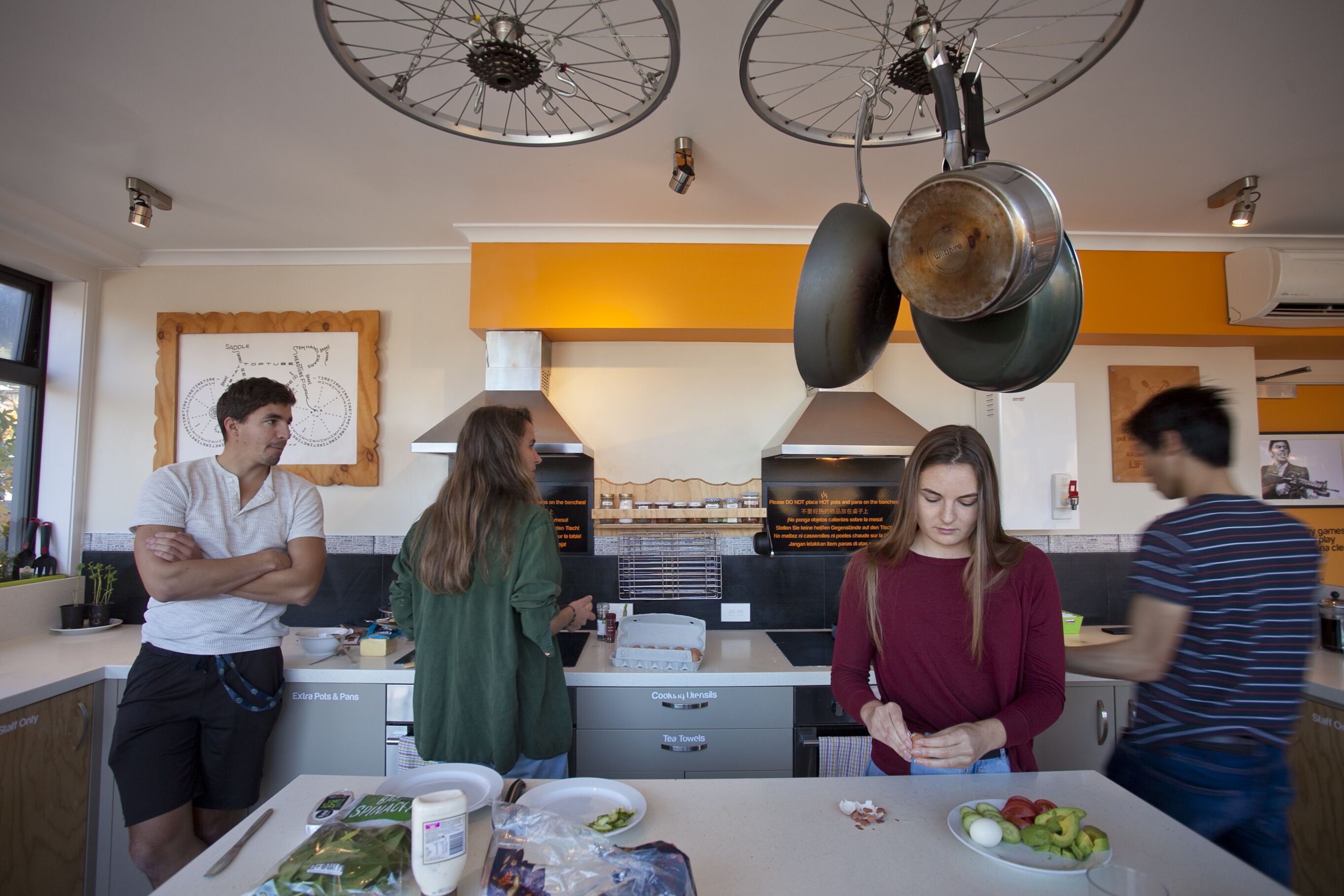 Een keuken met wanddecoratie met fietsenmotief, hangende pannen en een aanrecht met etenswaren.