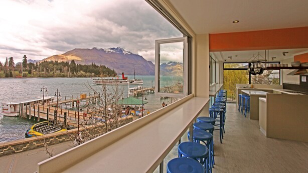 Un intérieur moderne offrant une vue sur un lac et des montagnes. Il comprend un coin bar avec des tabourets et un comptoir de cuisine.