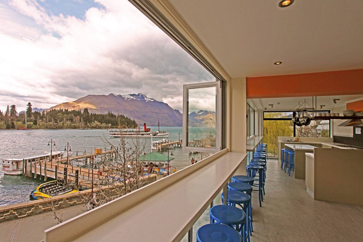 A modern interior with a view of a lake and mountains. It includes a bar area with stools and a kitchen counter.