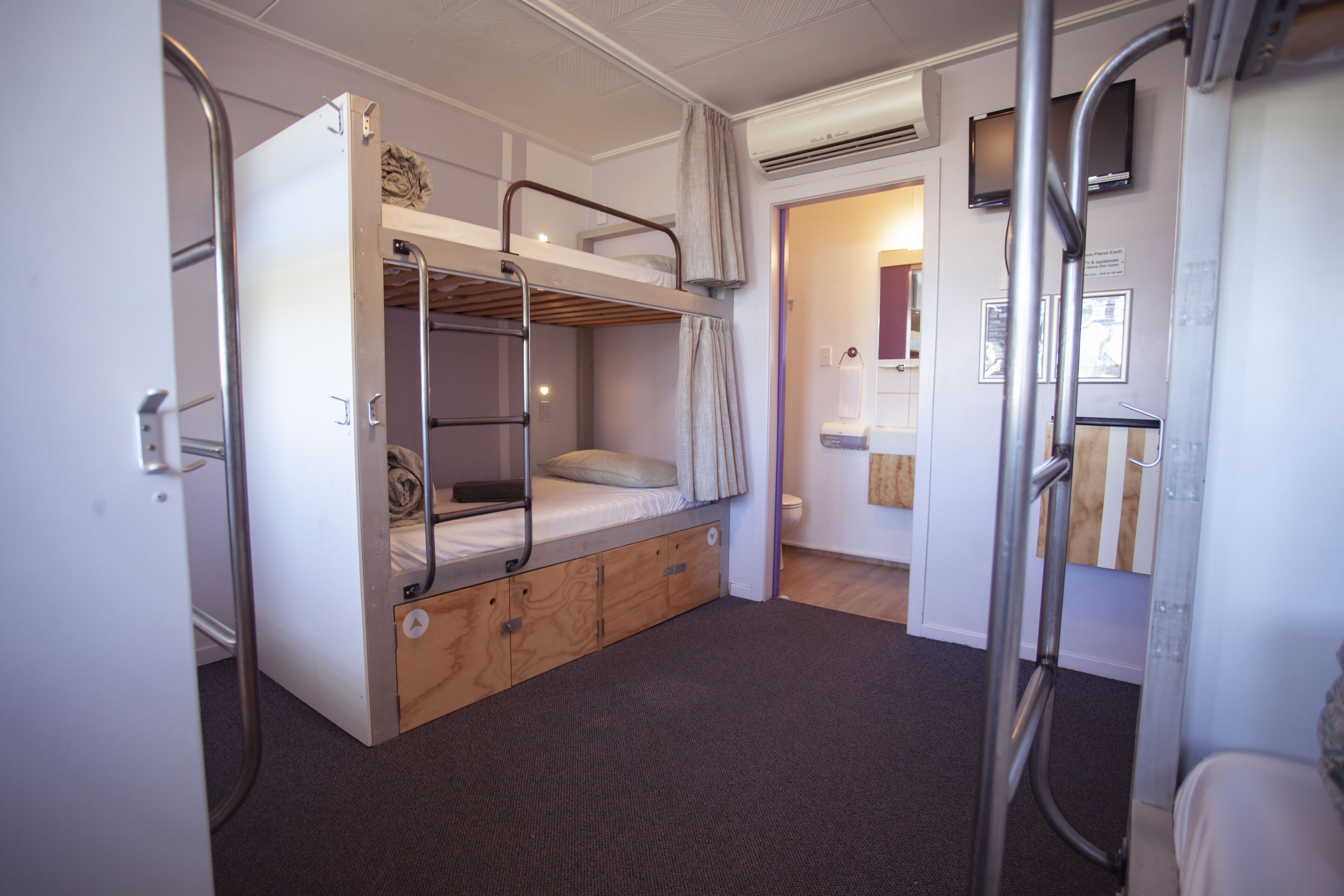 A bunk bed room with a wooden lower bunk, a pull-out desk, and a shower area with a towel rack.