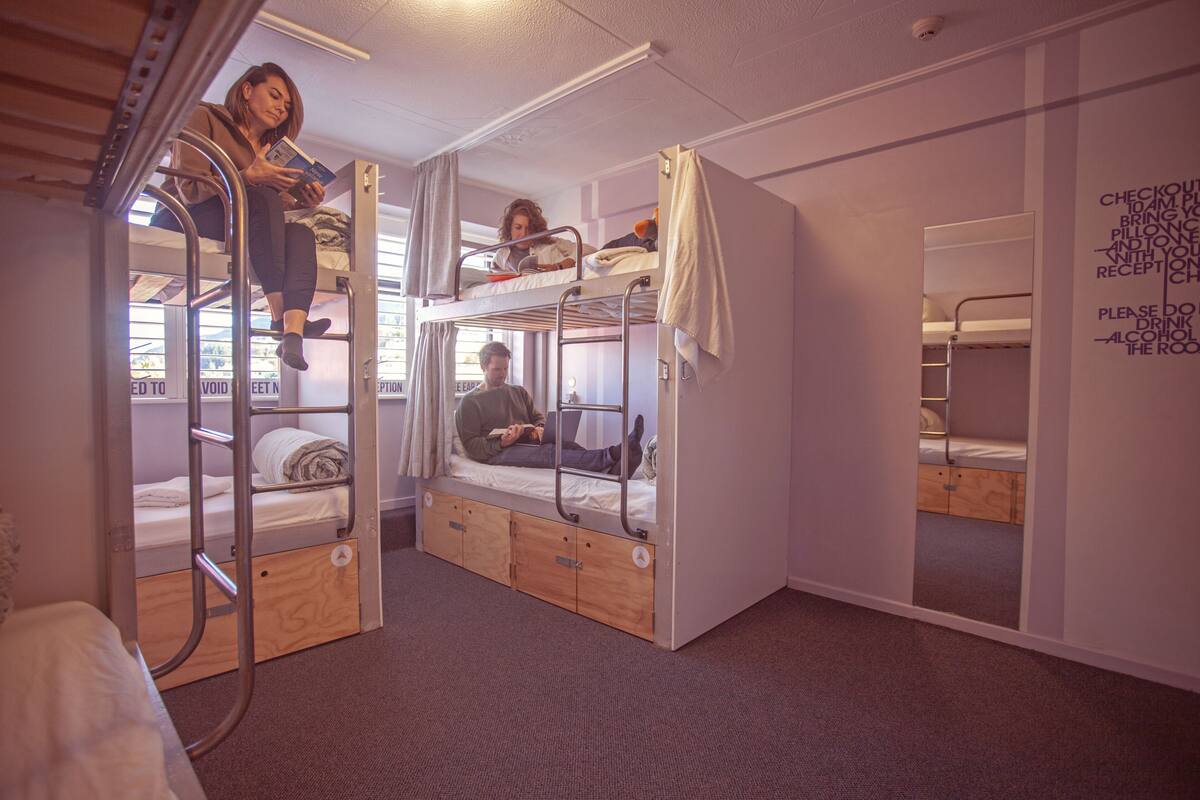 A dormitory-style room with bunk beds, a wooden wardrobe, and a mirror on the wall.