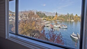 Une vue depuis une fenêtre donnant sur une rivière, avec des bateaux, des arbres et une chaîne de montagnes au loin.