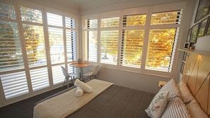 Une chambre à coucher avec un grand lit, une petite table, une chaise et une fenêtre avec des stores.