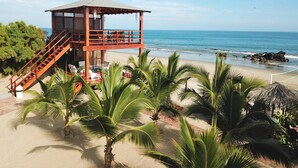 A beachside building with a staircase leading to an upper deck, surrounded by palm trees and overlooking the ocean. - Punta del Norte Bungalows (Canoas de Punta Sal)