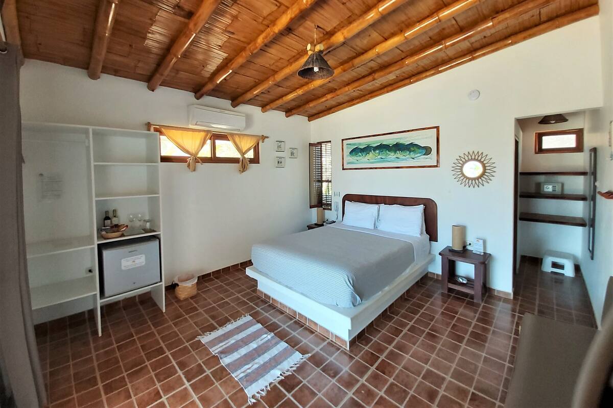Ein Schlafzimmer mit Holzboden, einem Bett mit weißer Bettwäsche, einem kleinen Nachttisch, einer Regaleinheit und einem Fenster mit Vorhängen.