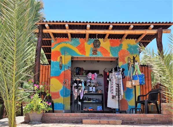 A colorful, rustic shop with a corrugated metal roof, wooden beams, and a variety of items displayed inside, including clothing and accessories.