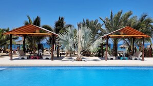 A poolside area with two wooden gazebos, lounge chairs, and a palm tree. - Punta del Norte Bungalows (Canoas de Punta Sal)