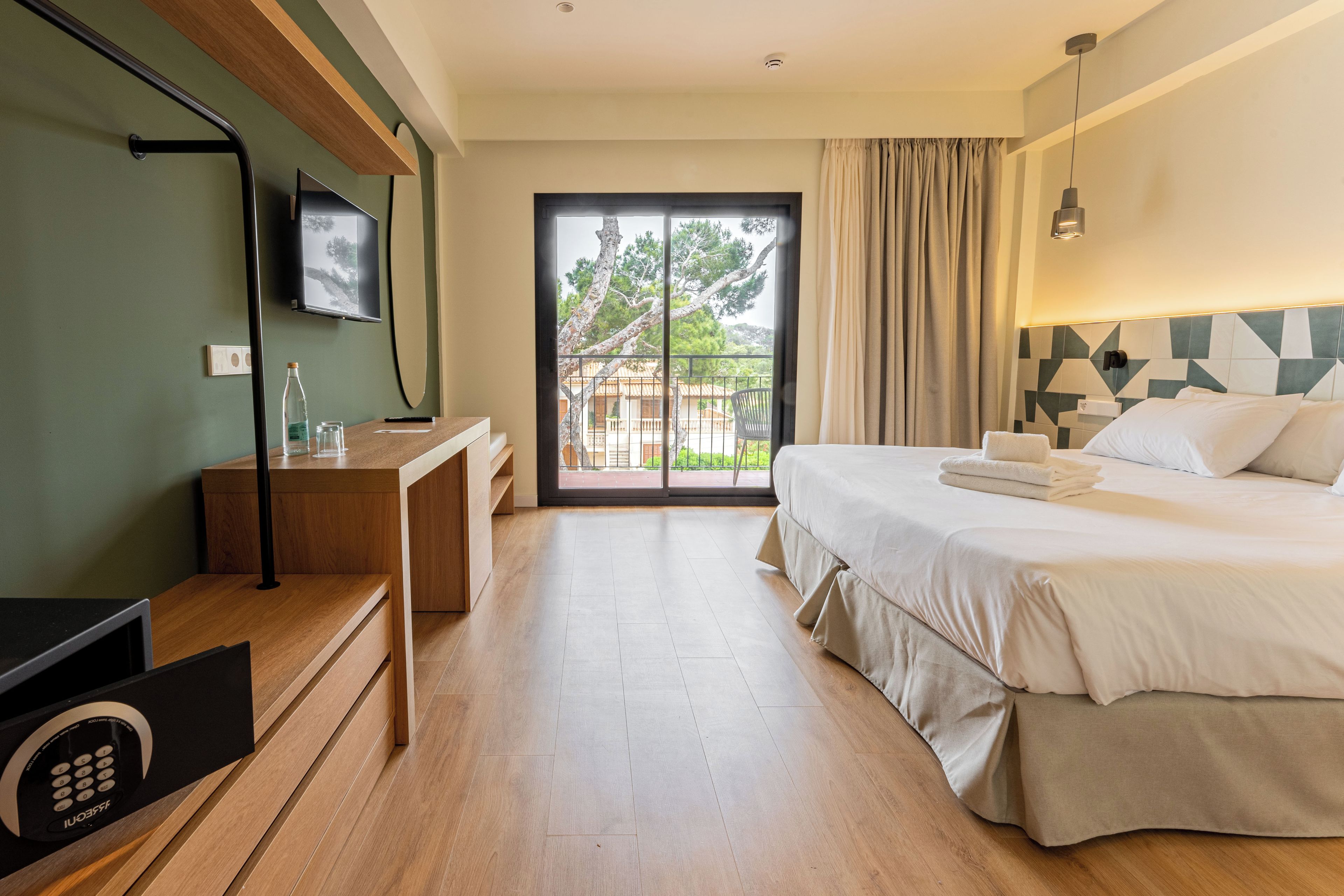 Una habitación de hotel con cama, escritorio, televisor y puerta corrediza de vidrio al exterior.