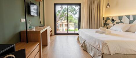Una habitación de hotel con cama, escritorio, televisor y puerta corrediza de vidrio al exterior.