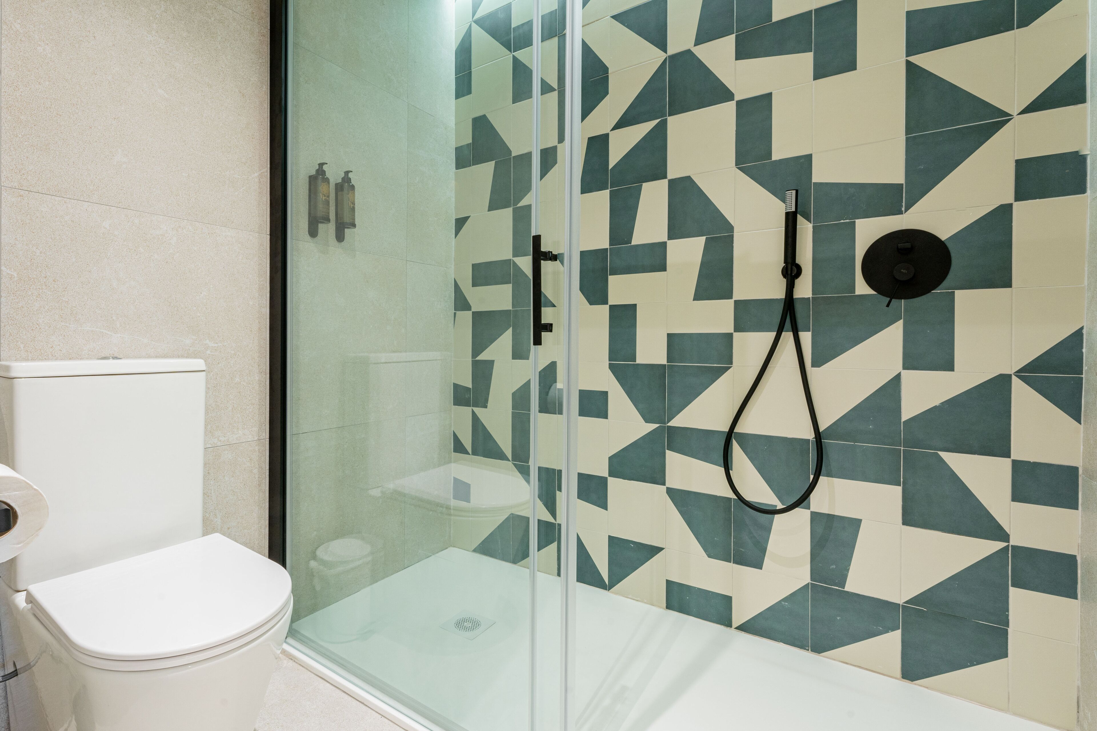 Een moderne badkamer met een douchecabine van glas, een toilet en een behang met een patroon.