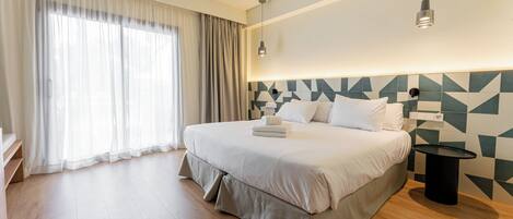 A modern hotel room with a large bed, a bedside table, a wall-mounted lamp, and a window with curtains.