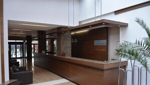 A modern reception area with a wooden reception desk, a seating area with leather sofas, and a large potted plant.