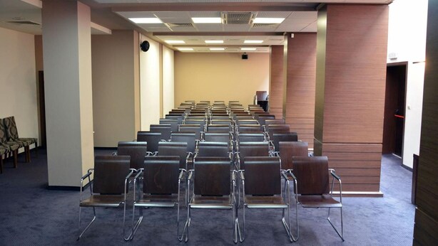 A conference room with rows of chairs, a projector, and a clock on the wall.