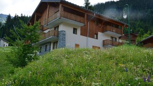 A multi-story wooden chalet with balconies, surrounded by lush greenery and wildflowers. - Vacancéole - Les Chalets de la Ramoure (Modane)