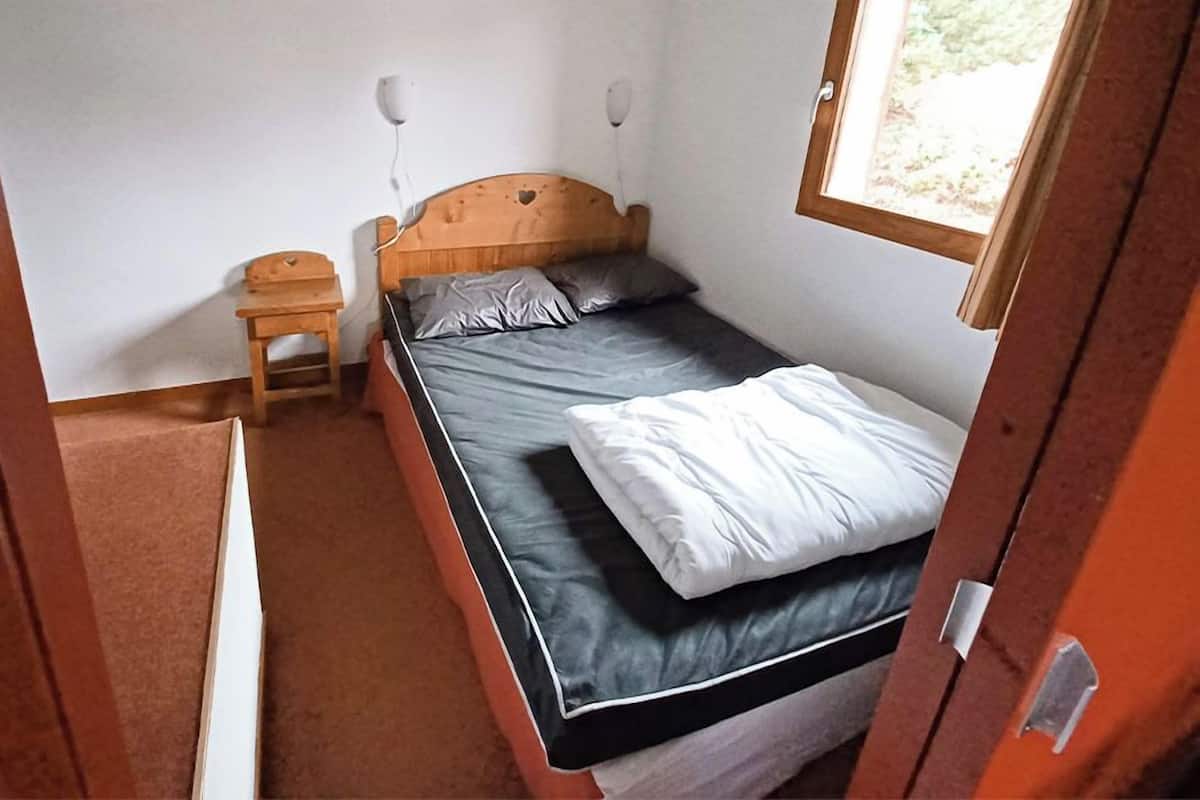 Una habitación pequeña con cama individual, cabecera de madera, mesita de noche y ventana.