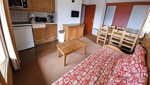 A compact room with a bed, a wooden table, a small kitchen area with a microwave, a coffee maker, and a TV. - Vacancéole - Les Chalets de la Ramoure (Modane)
