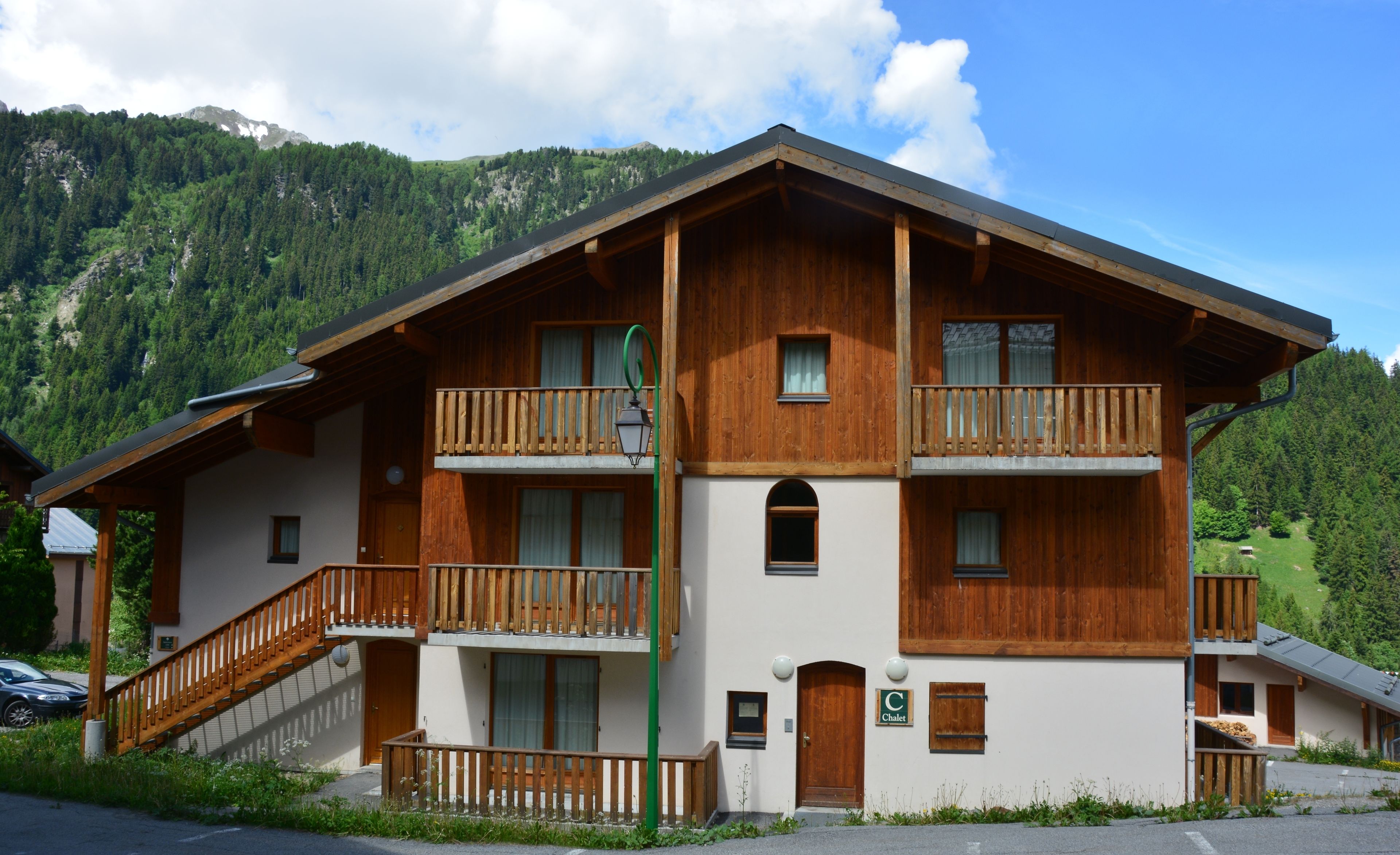 A two-story chalet with wooden balconies, a staircase, and a view of a mountainous landscape.