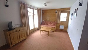 A room with a wooden sofa, a small table, a TV on a wooden cabinet, and a window with curtains. - Vacancéole - Les Chalets de la Ramoure (Modane)