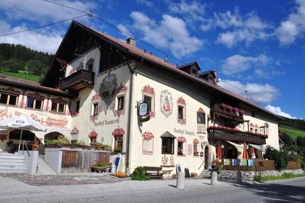A traditional Alpine-style building with a balcony, a sign reading "Gasthof Neubirth," and outdoor seating with umbrellas.