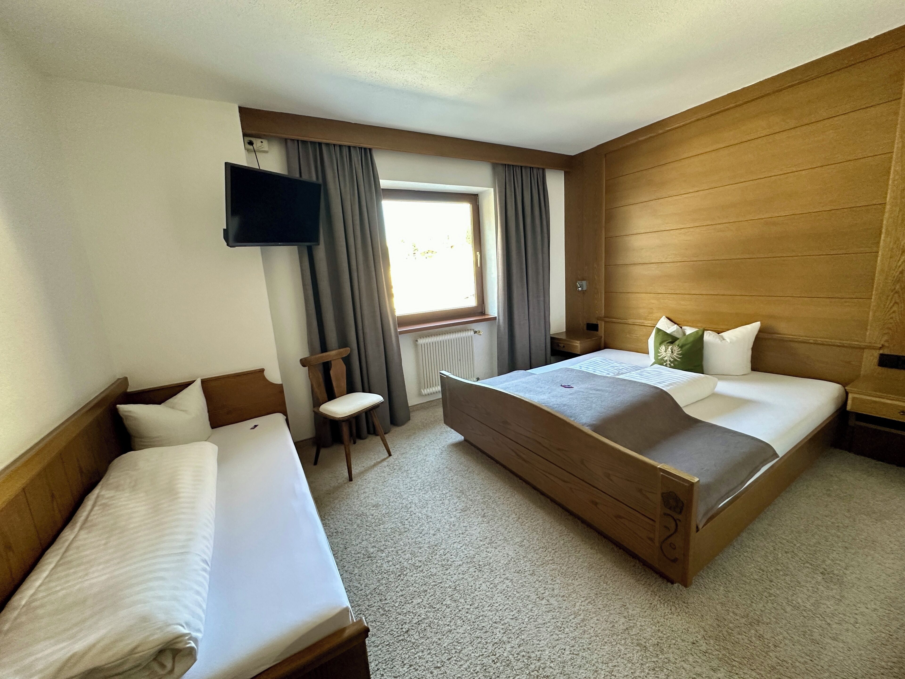 A hotel room with two beds, a TV, a window with curtains, and a radiator.