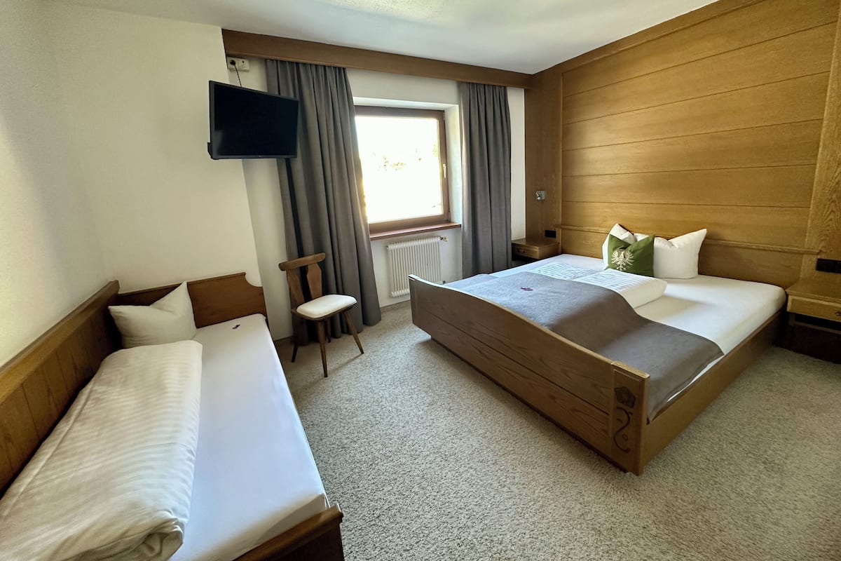 A hotel room with two beds, a TV, a window with curtains, and a radiator.
