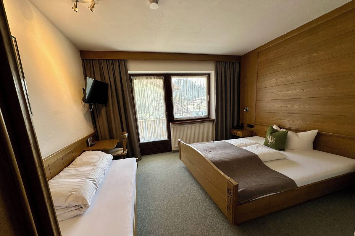Habitación de hotel con dos camas individuales, cabecero de madera, televisor, ventana con cortinas y radiador.