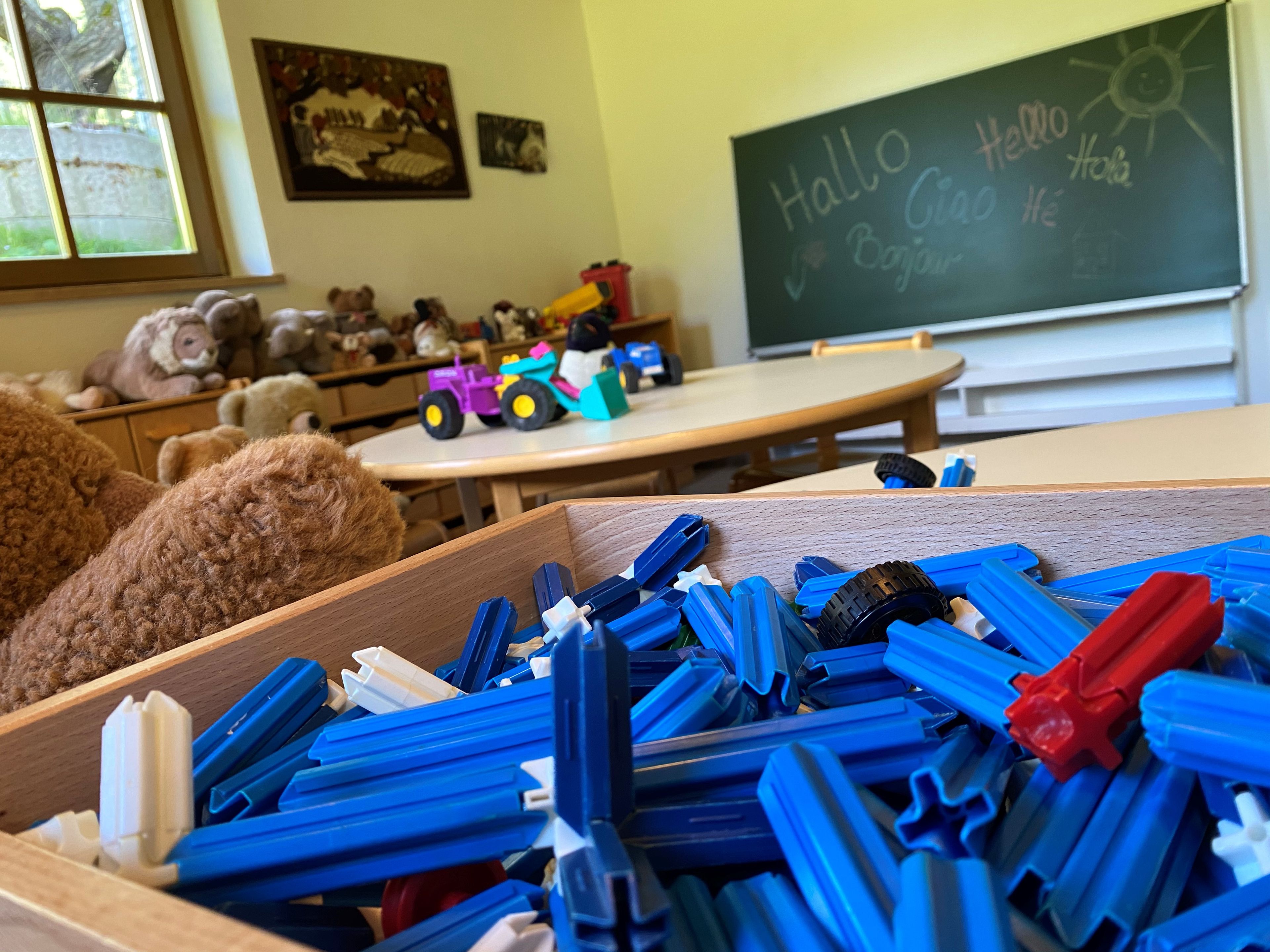 A classroom with educational toys, a chalkboard with 'Hello' written on it, and a window with a view of trees.