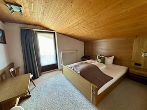 Una habitación con techo de madera, una cama con almohadas, una silla, una mesa y una ventana con cortinas.
