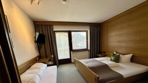 Habitació d'hotel amb dos llits individuals, un capçal de llit de fusta, una televisió, una finestra amb cortines i un radiador.