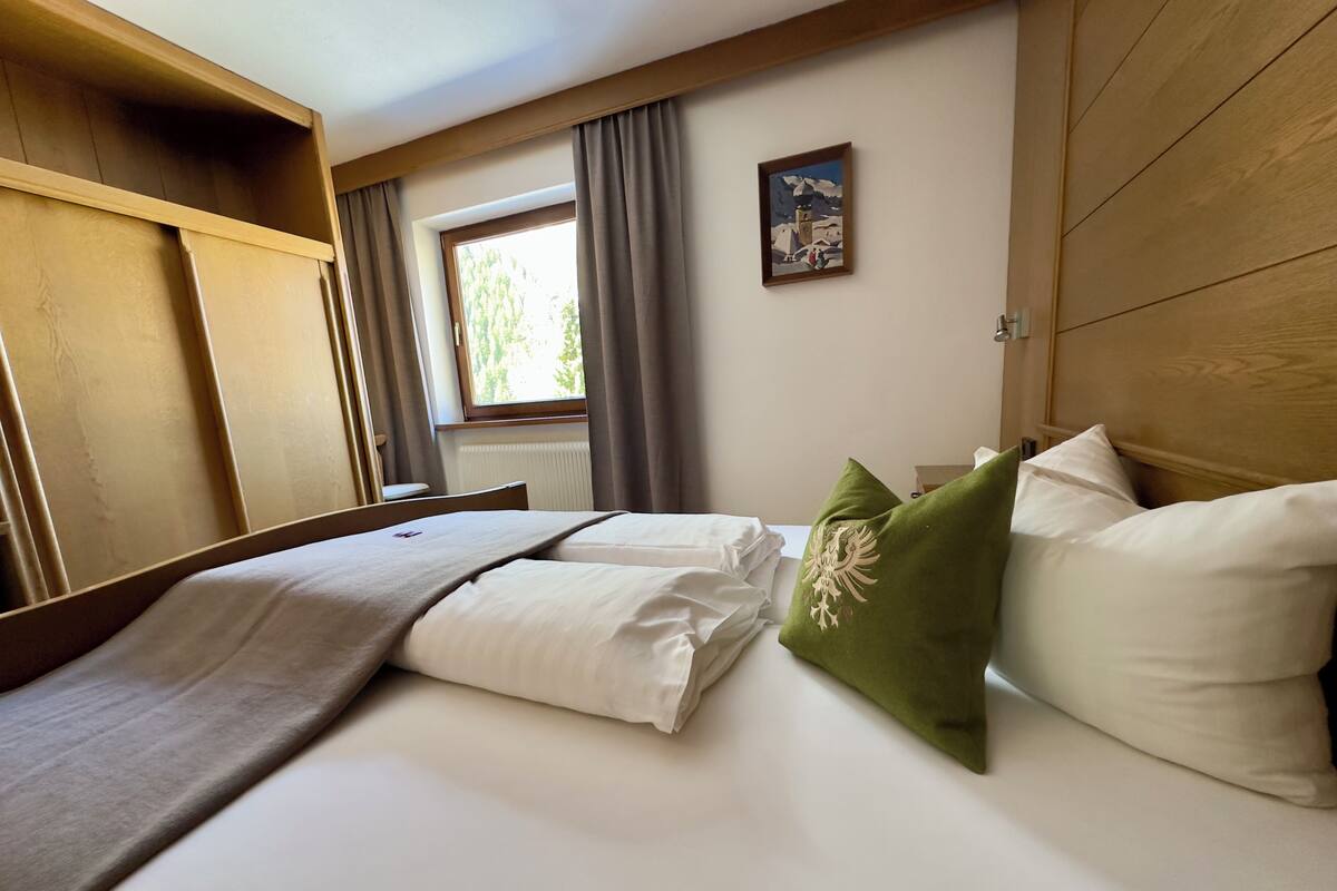 Habitación de hotel con una cama, cabecera de madera, ventana con cortinas y un cuadro en la pared.