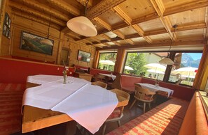A wooden interior with tables set for dining, benches, and a view of the outdoors.