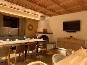 Un comedor con una mesa de madera larga, sillas, una chimenea y un televisor montado en la pared.