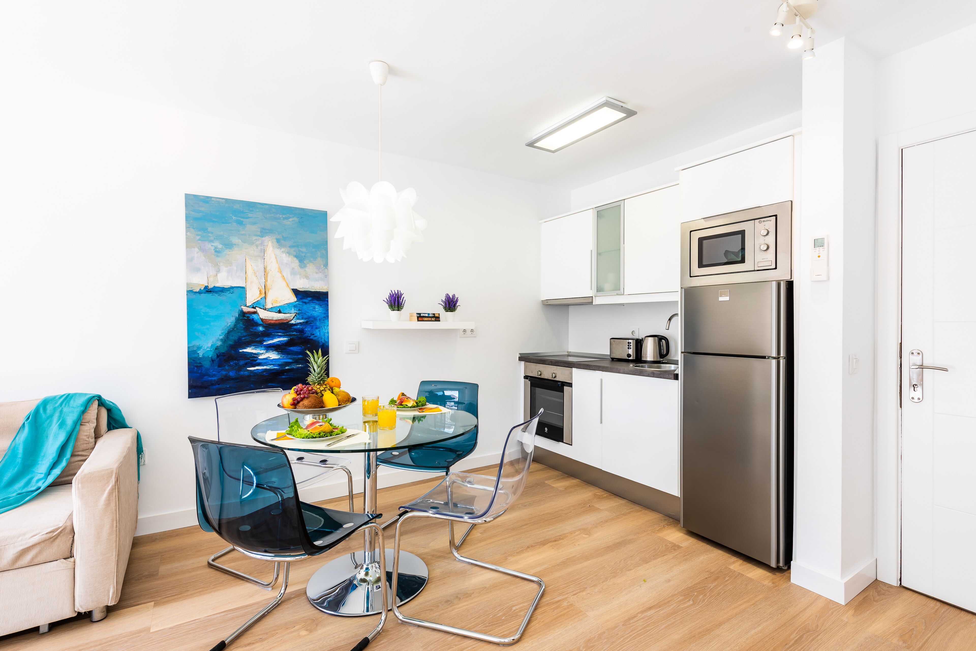 A modern kitchen with white cabinets, stainless steel appliances, and a glass dining table with chairs.