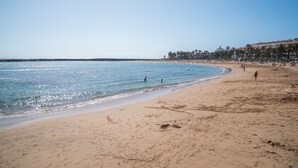 Une plage avec une eau d’un bleu limpide, un rivage sablonneux et une rangée de bâtiments le long de la côte.