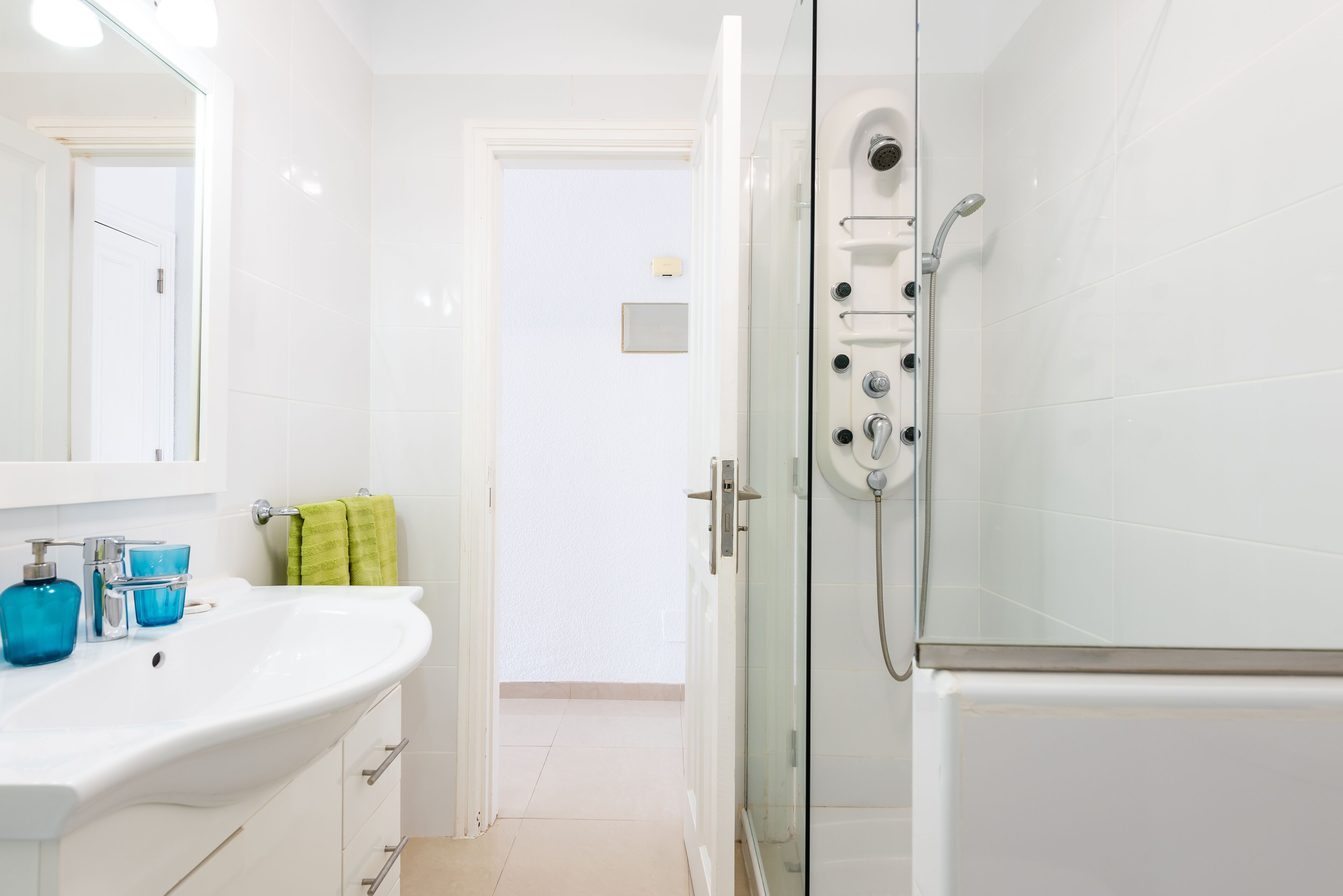 A bathroom with a white sink, a glass shower enclosure, and a door leading to another room.