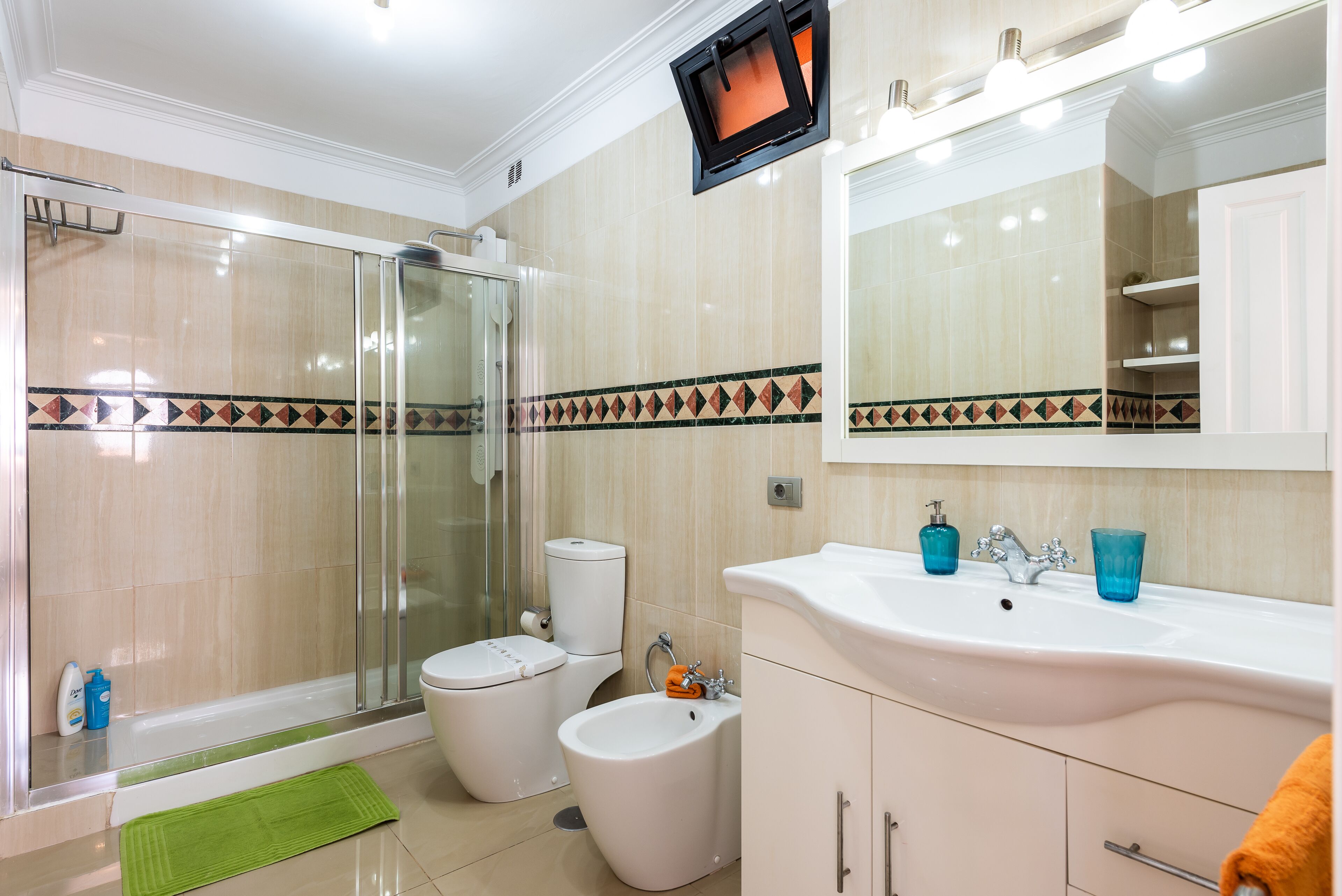 A modern bathroom with a glass shower enclosure, a toilet, a bidet, and a sink with a mirror above.
